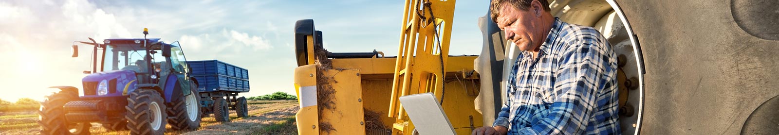 A farmer using a laptop computer around farming equipment